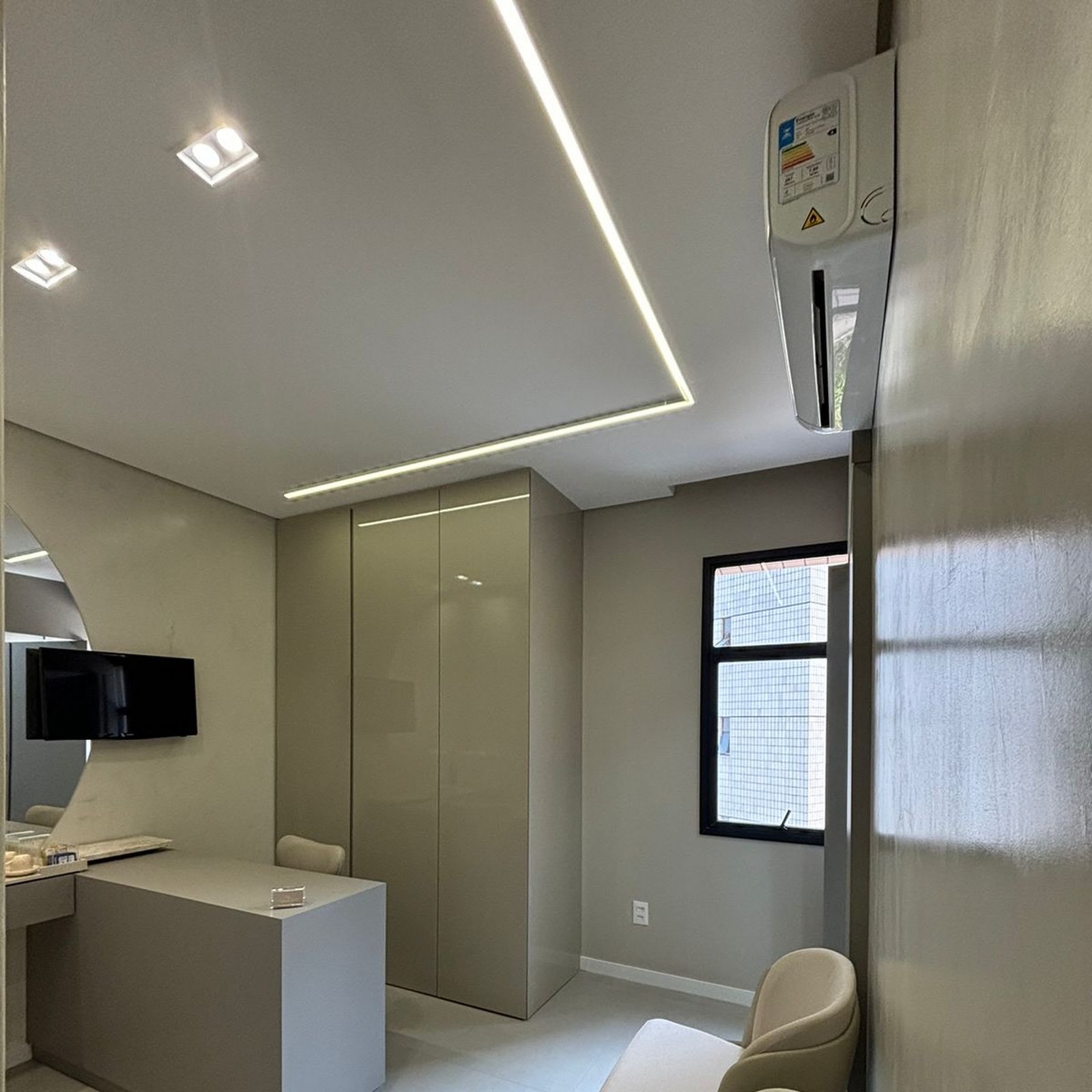 Detalhe do consultório: mobiliário claro, armário planejado e iluminação em fita no teto